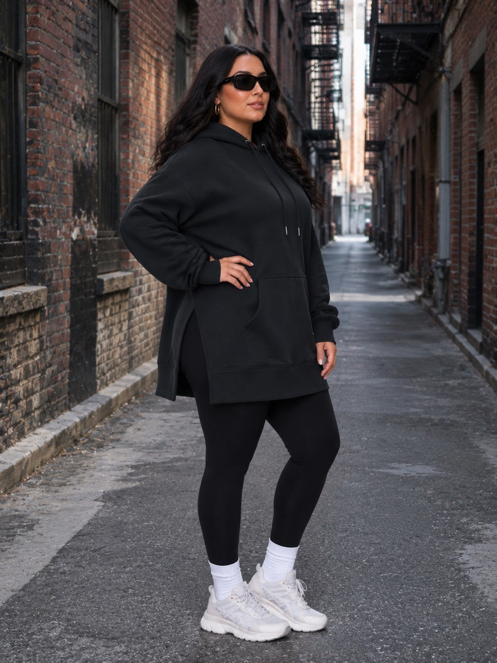 Woman wearing a black Warmy, leggings and sneakers on a brick-lined street