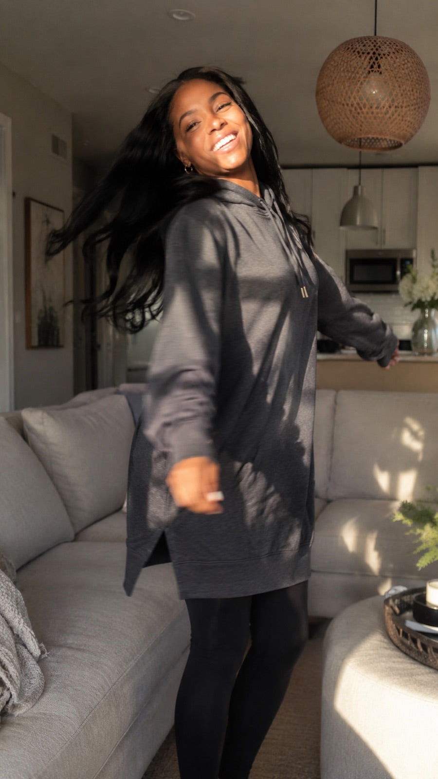 Woman wearing a charcoal Warmy and leggings beside her sofa